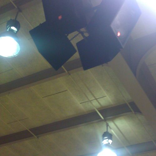 Speakers mounted to overhead beam in school gym.