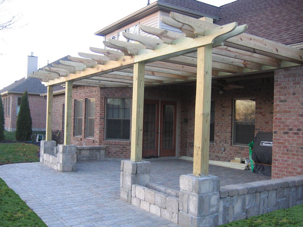 Patio with unstained pergola. Flower beds and seat