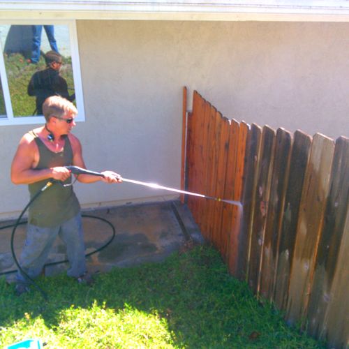 Matthew is power-washing a fence, on the left is a