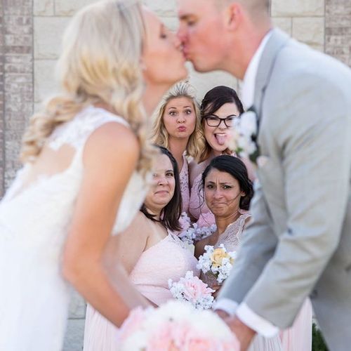 Couple kissing while bridesmaids make silly faces 