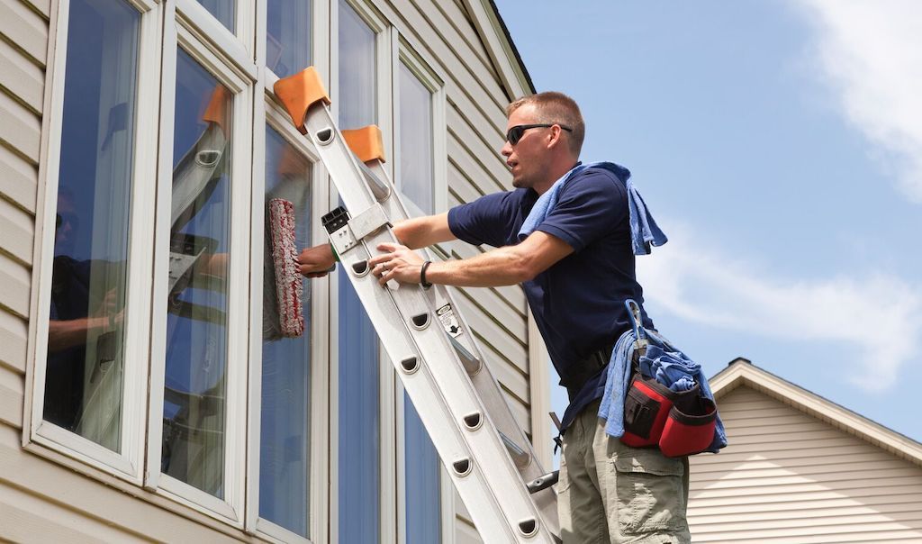 man washing exterior windows on ladder