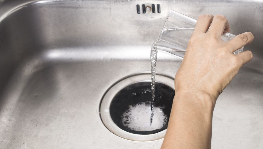 pouring baking soda mixture into kitchen sink to unclog it