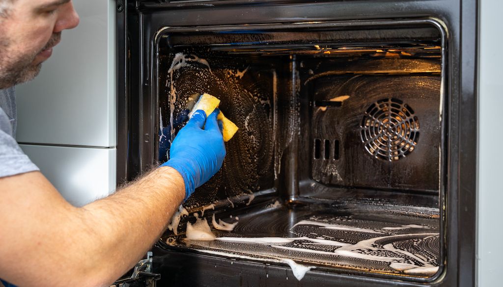 man cleaning inside of oven