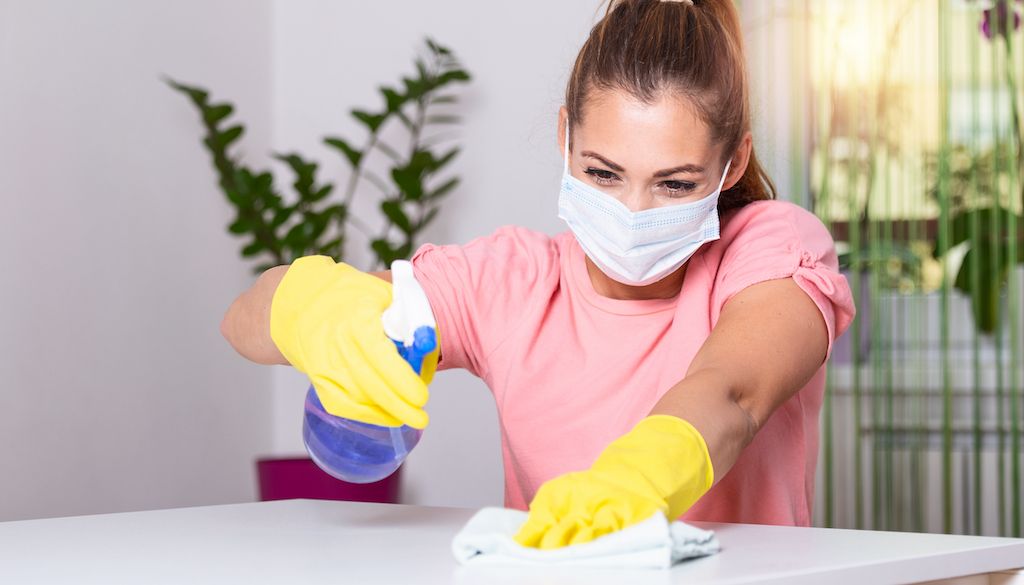 woman with mask and gloves on cleaning table