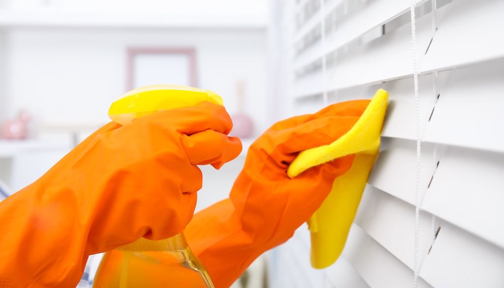 orange gloves spraying and wiping down window blinds