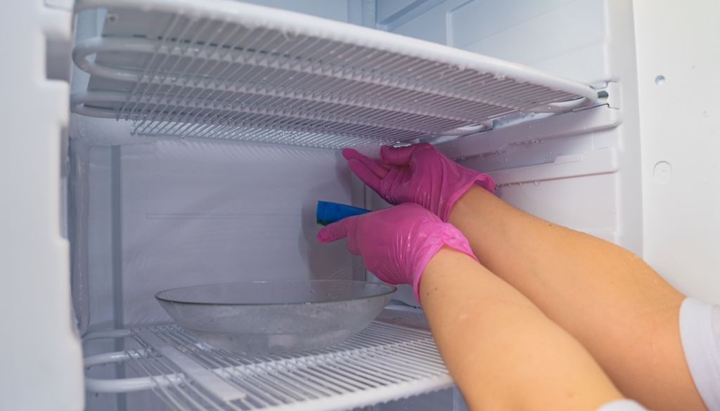 person with pink gloves defrosting and cleaning freezer
