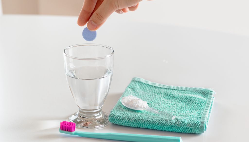 hand putting denture tables in glass of water next to toothbrush