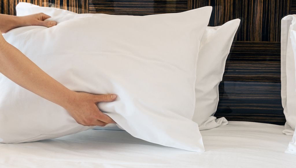 hands placing pillow on bed