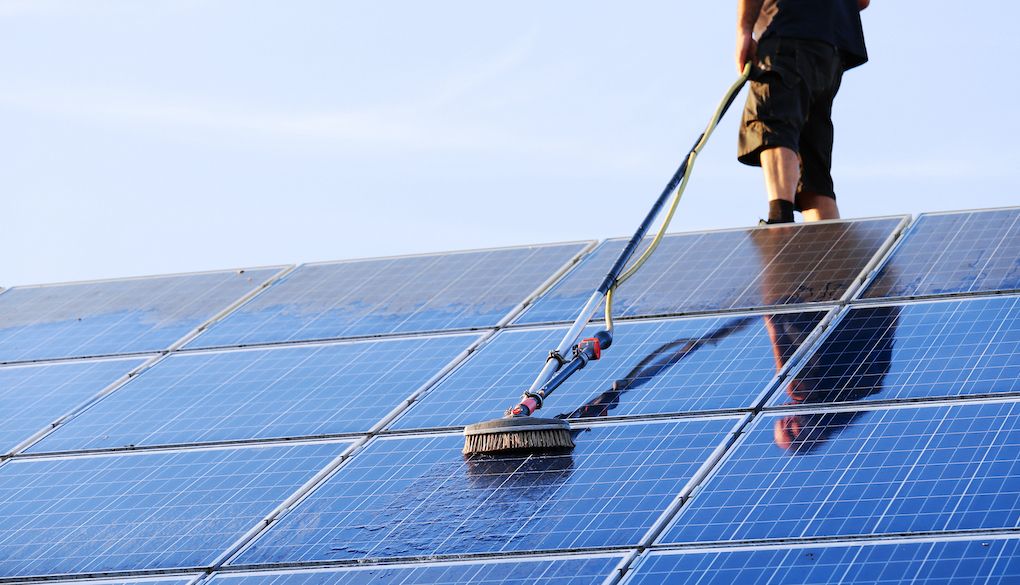 person cleaning solar panels on roof