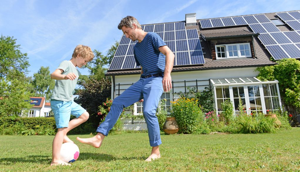 man and boy playing soccer in front of house with solar panels on roof
