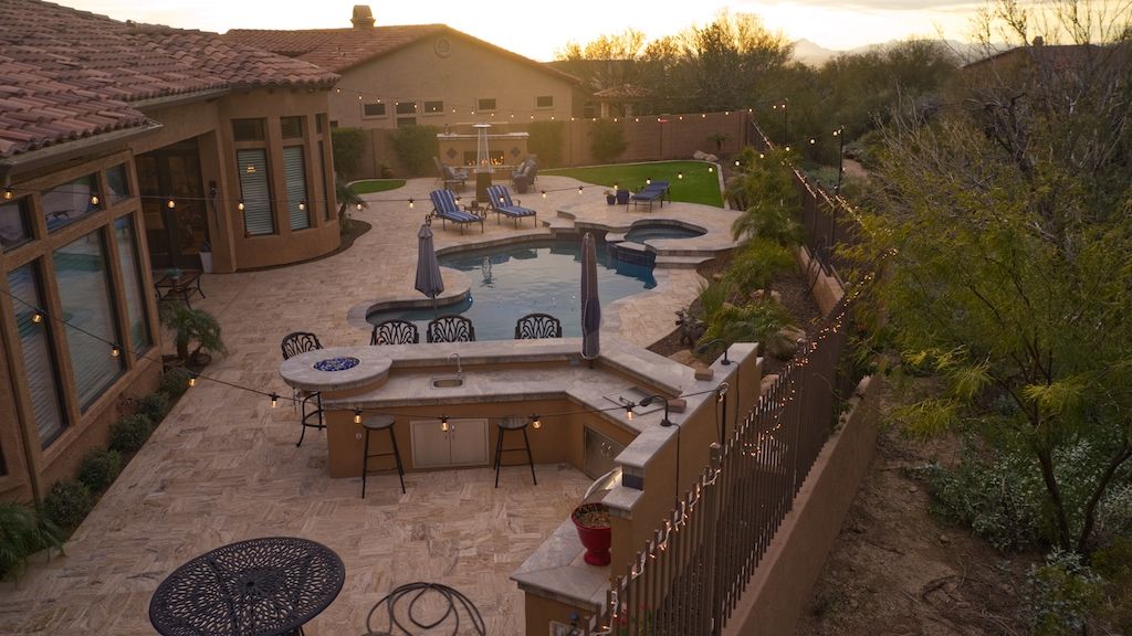 outdoor kitchen and dining near swimming pool in backyard with string lights