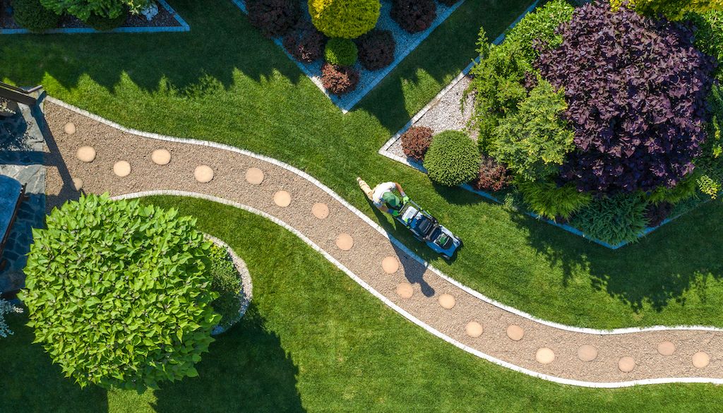 aerial view of backyard landscape with gardener mowing the lawn