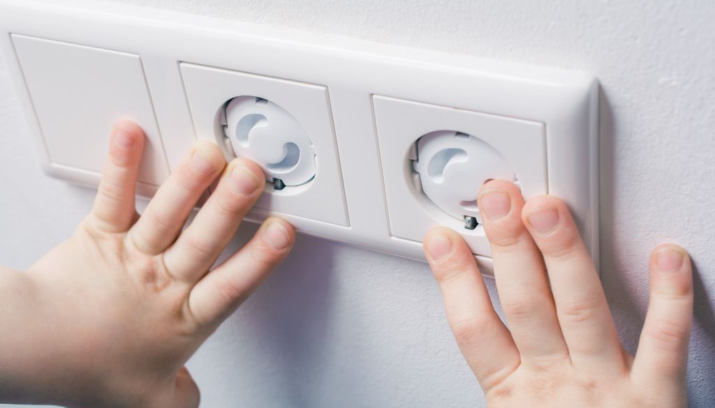 child hands touching wall socket outlet with safety plugs