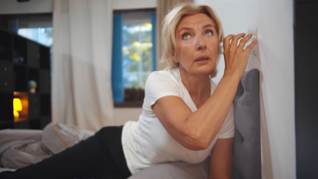 woman holding cup up to wall to listen to strange sounds