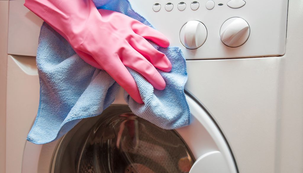 gloved hand wiping down washing machine exterior