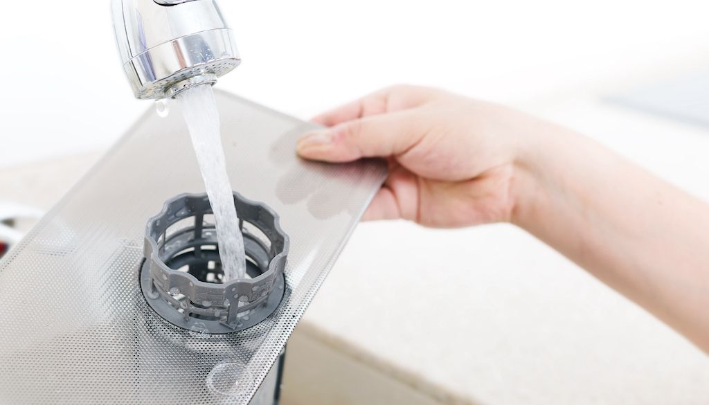 rinsing dishwasher filter in water in kitchen sink
