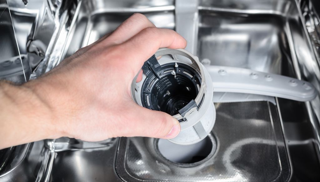 hand putting the dishwasher filter back into its housing