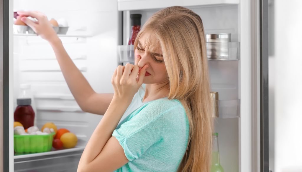 woman plugging nose when opening door to smelly fridge
