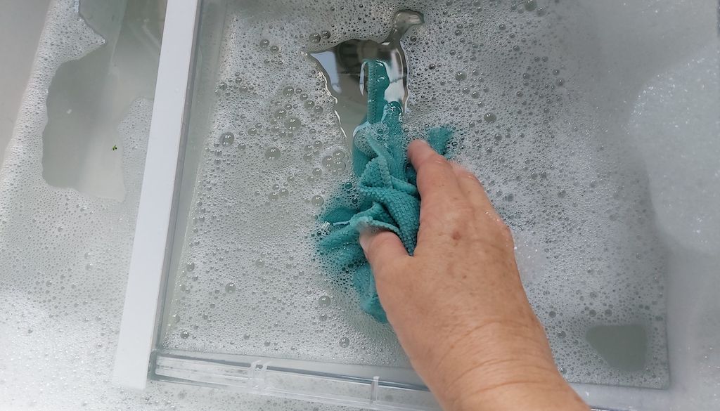 cleaning fridge drawer and trays in kitchen sink