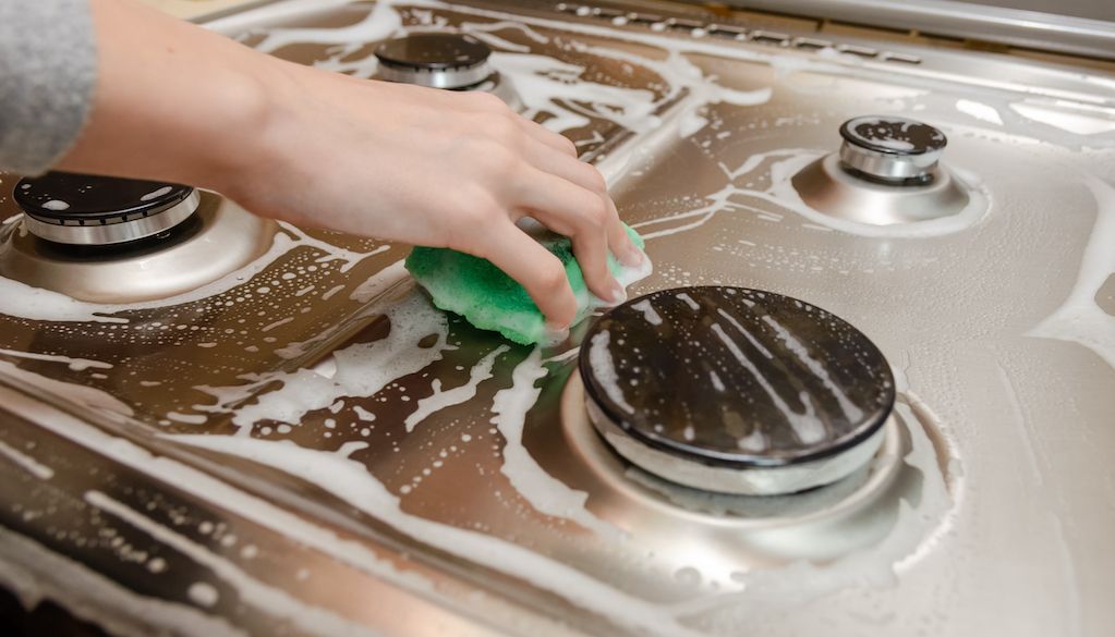 hands cleaning stainless steel gas stove top