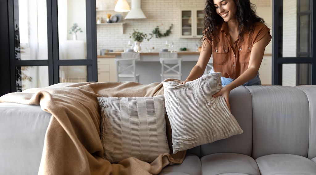 woman placing pillows and blankets on couch