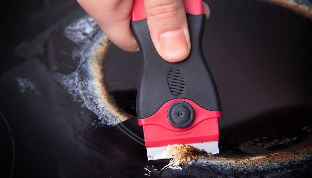 scraper being used to remove grime on stovetop