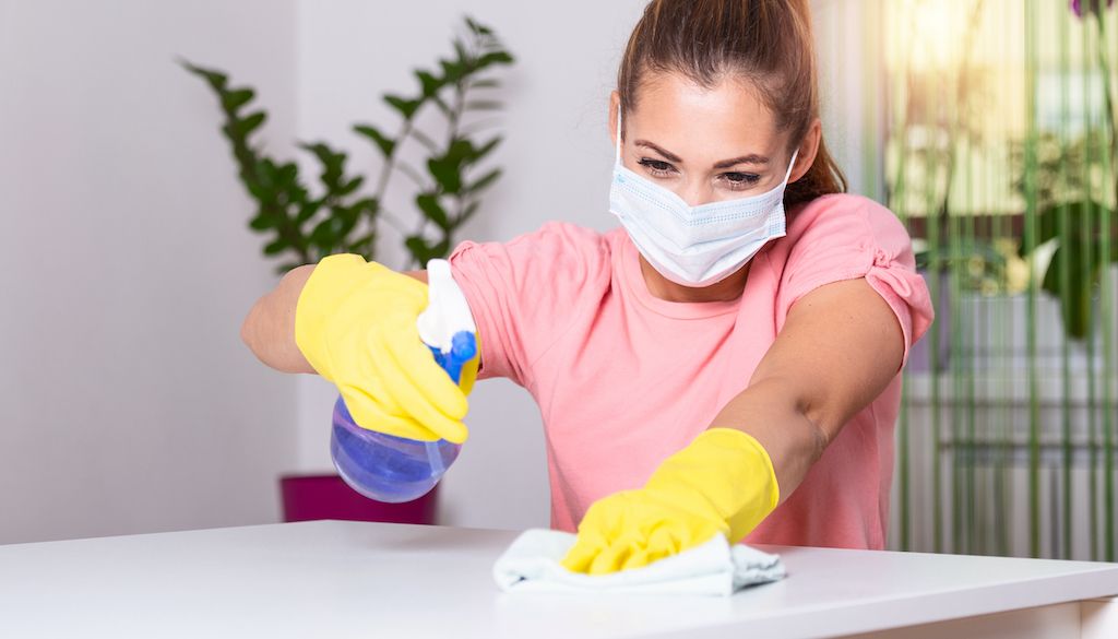 woman with rubber gloves and face mask cleaning table