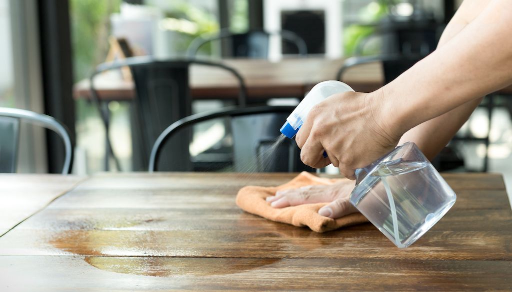 spraying cleaner on table and wiping it off