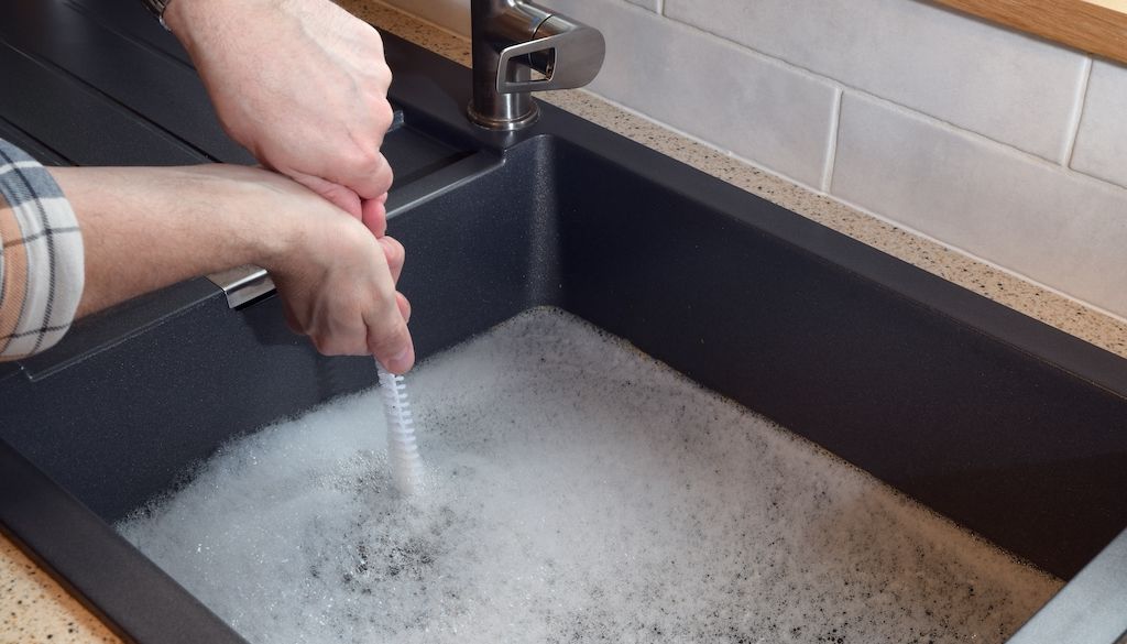 plumber using snake to unclog overflowing kitchen sink