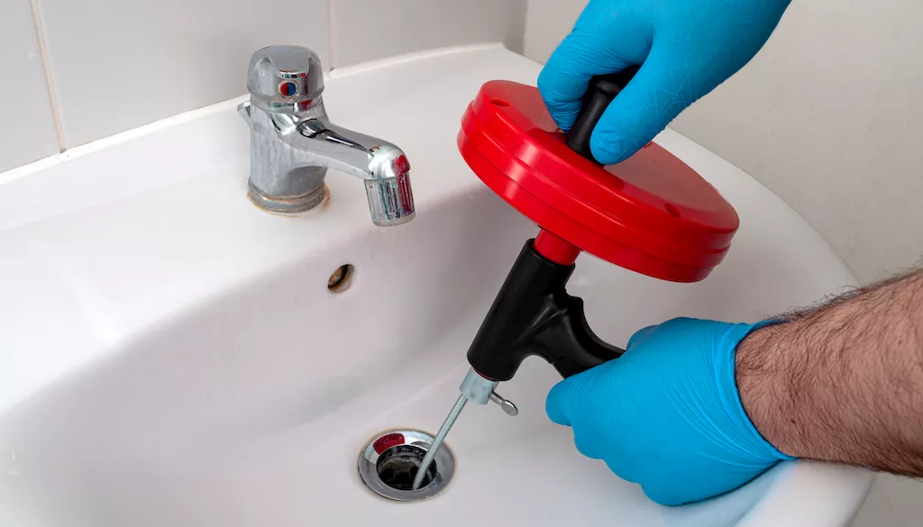 person using plumbing snake to clear bathroom sink clog