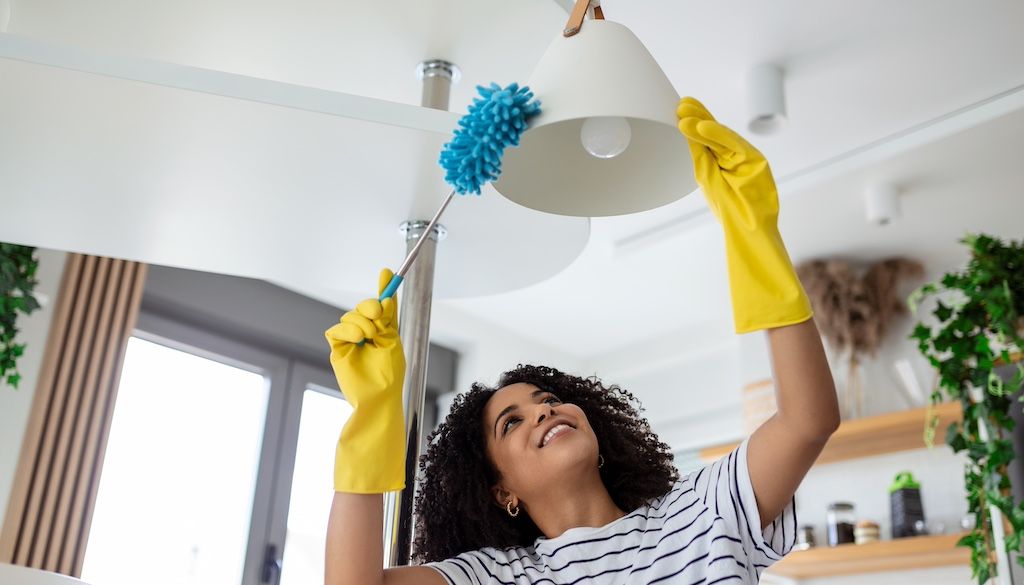 woman dusting and cleaning ceiling light fixture
