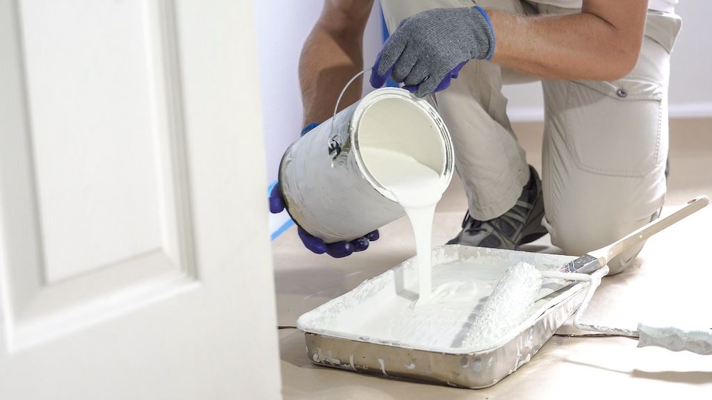 painter pouring white paint in tray