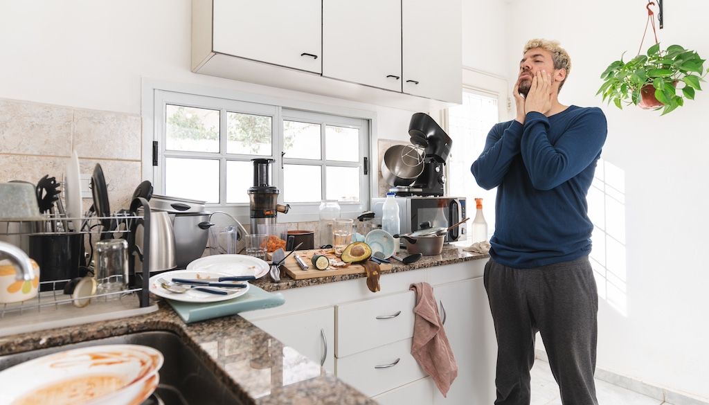 stressed man in kitchen looking at dirty dishes