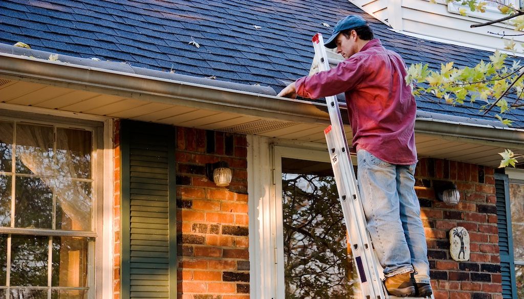 man on ladder cleaning gutters on two story home